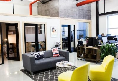 Lounge area with grey sofa, yellow chairs, and modern glass-walled offices.