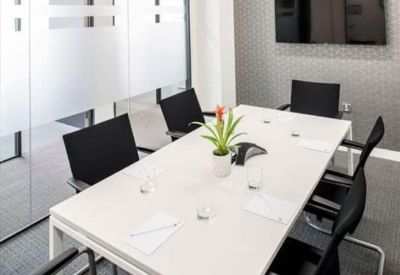 Professional meeting room with a white conference table, black chairs, and a wall-mounted screen.