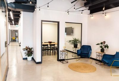 Reception area and waiting lounge featuring blue velvet armchairs, potted plants, and warm string lighting.