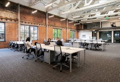 Spacious coworking area with brick walls, exposed ceilings, and long communal tables.