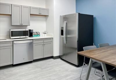 Modern office breakroom with grey cabinetry and stainless steel appliances.
