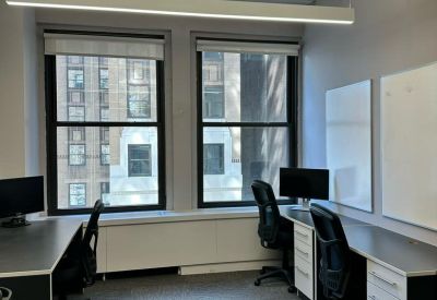 Bright office with two rows of desks, whiteboards, and large windows with city views.