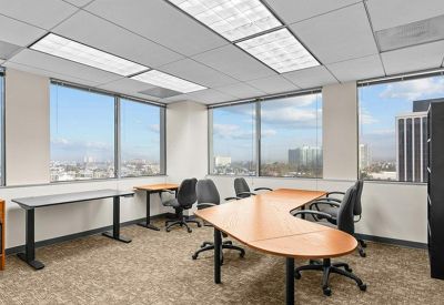 Bright corner office with multiple desks, black chairs, and city views.