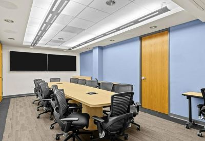 Meeting room with a long table, black chairs, and digital screens.