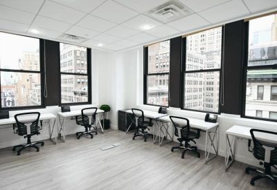 Bright open-plan office area with white desks and large windows overlooking the city.