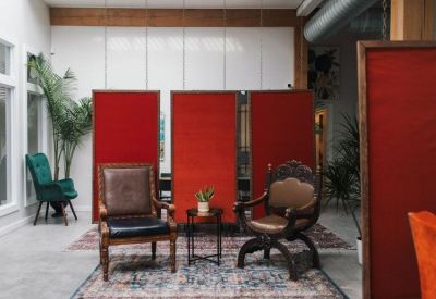 Breakout lounge with red privacy screens, vintage chairs, and a teal velvet armchair.