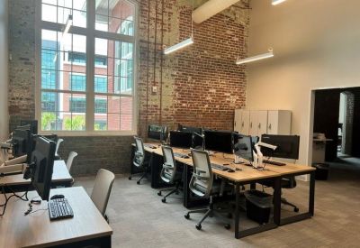 Sunlit office workspace featuring exposed brick walls and large industrial windows.