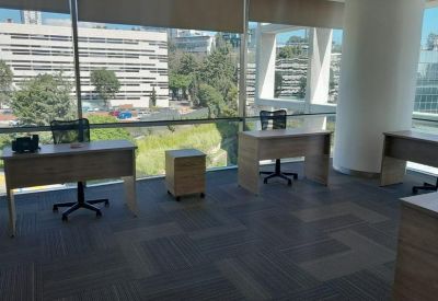 Bright corner office with three wooden desks and large windows overlooking the city.