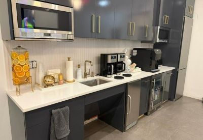 Sleek office kitchen with dark cabinetry, coffee machines, and marble countertops.