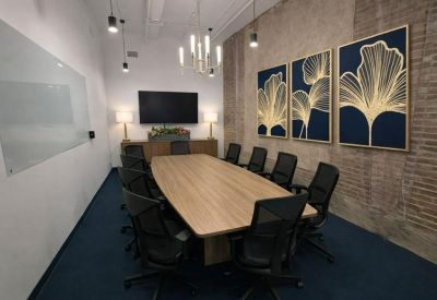Modern boardroom featuring a long wooden table, blue carpet, and gold leaf wall art.