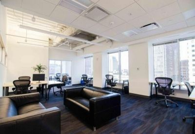 Open-plan office featuring black leather sofas and multiple workstations.