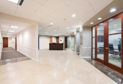 Bright office hallway leading to a central reception desk and wood-framed glass doors.