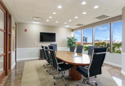Formal boardroom with a large wood table, black leather chairs, and expansive window views.
