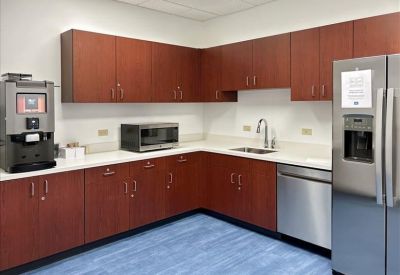 Modern breakroom kitchen with wood cabinets, stainless steel appliances, and blue flooring.