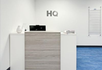 Reception desk with a light wood front and HQ logo on the back wall.