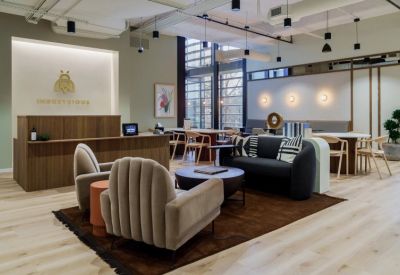Bright reception area featuring a wood-slat desk, modern armchairs, and Industrious branding on the wall.
