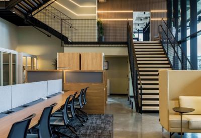 Bi-level office space featuring workstations, a high-back sofa, and a staircase leading to a mezzanine.