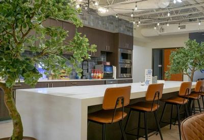 Spacious communal kitchen with a large white island, bar stools, and lush indoor trees.