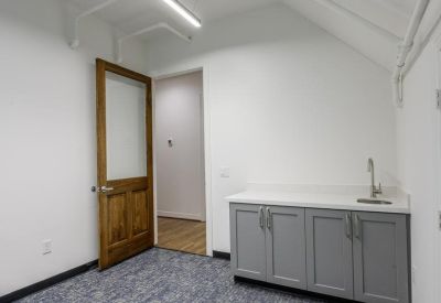 Private office suite with a wood-framed glass door and a small grey kitchenette unit.