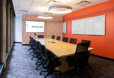 Boardroom with a long wooden table, black chairs, and a vibrant orange feature wall.