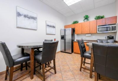 Modern breakroom kitchen with wood cabinetry, stainless steel fridge, and dining tables.