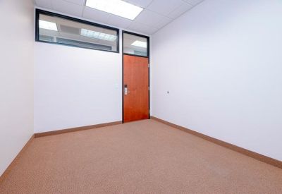Empty private office with neutral walls and a solid wood door with a glass transom.
