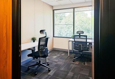 Private two-person office suite with white desks and large windows overlooking trees.