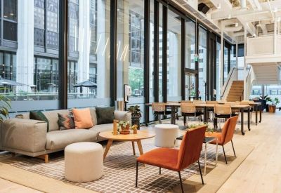 Bright lounge area featuring orange armchairs, a gray sofa, and floor-to-ceiling windows.