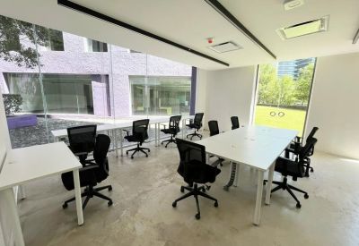 Bright open-plan office space with white desks and black mesh chairs near large windows.
