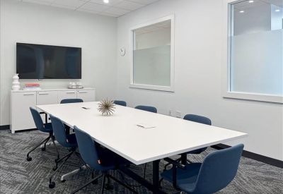 A professional conference room featuring a large white table, blue chairs, and a wall-mounted monitor.