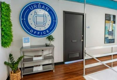 Bright reception area with wood floors, a round branded wall sign, and a decorative plant.
