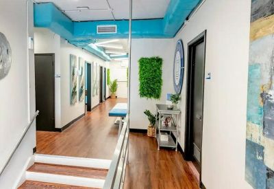 Bright hallway featuring hardwood floors, teal accents, indoor plants, and a small breakout area.