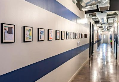 Bright hallway with blue accent stripes, framed artwork, and industrial exposed ductwork.
