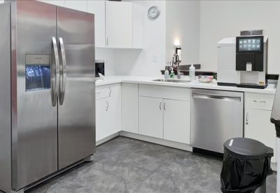 Bright office kitchen with stainless steel appliances and white cabinetry.