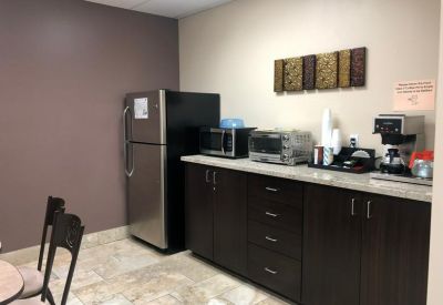 Office breakroom featuring a dark wood kitchenette, stainless steel fridge, and coffee station.