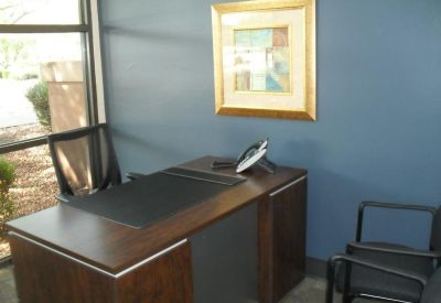 Private office suite with a dark wood desk, guest chairs, and framed wall art.