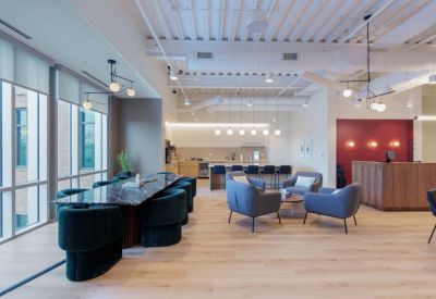 Spacious coworking lounge with a marble communal table, teal velvet chairs, and a modern kitchen area.