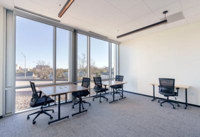 Bright open-plan workspace with multiple wooden desks and large windows overlooking the city.