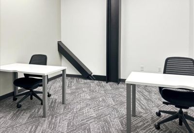 Bright workspace featuring two white desks and black chairs against a neutral wall with architectural pillars.