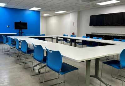 Spacious meeting room with a U-shaped white table, blue chairs, and a vibrant blue feature wall.