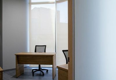 Private office suite with a wooden desk and mesh chair against a large window.