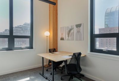 Small private office with two desks, mesh chairs, and large windows.