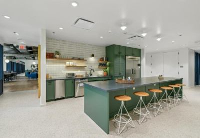 Spacious communal kitchen with green cabinetry, wood shelving, and island seating.