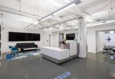 Modern reception area with a white desk, grey flooring, and blue patterned rug.