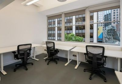 Bright corner workspace with three white desks and ergonomic black chairs.