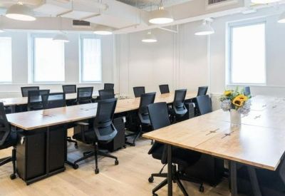 Bright open-plan office with long wooden desks and ergonomic black chairs.