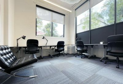 Bright workspace with multiple desks, black rolling chairs, and large windows.