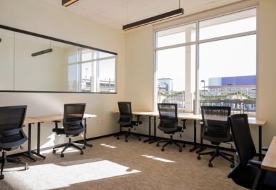 Bright open-plan workspace with multiple desks, ergonomic chairs, and large windows.