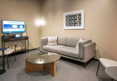 Modern lounge area with a grey sofa, glass coffee table, and wall-mounted TV screen.