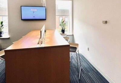 Coworking bench with integrated power and a wall-mounted monitor near a window.